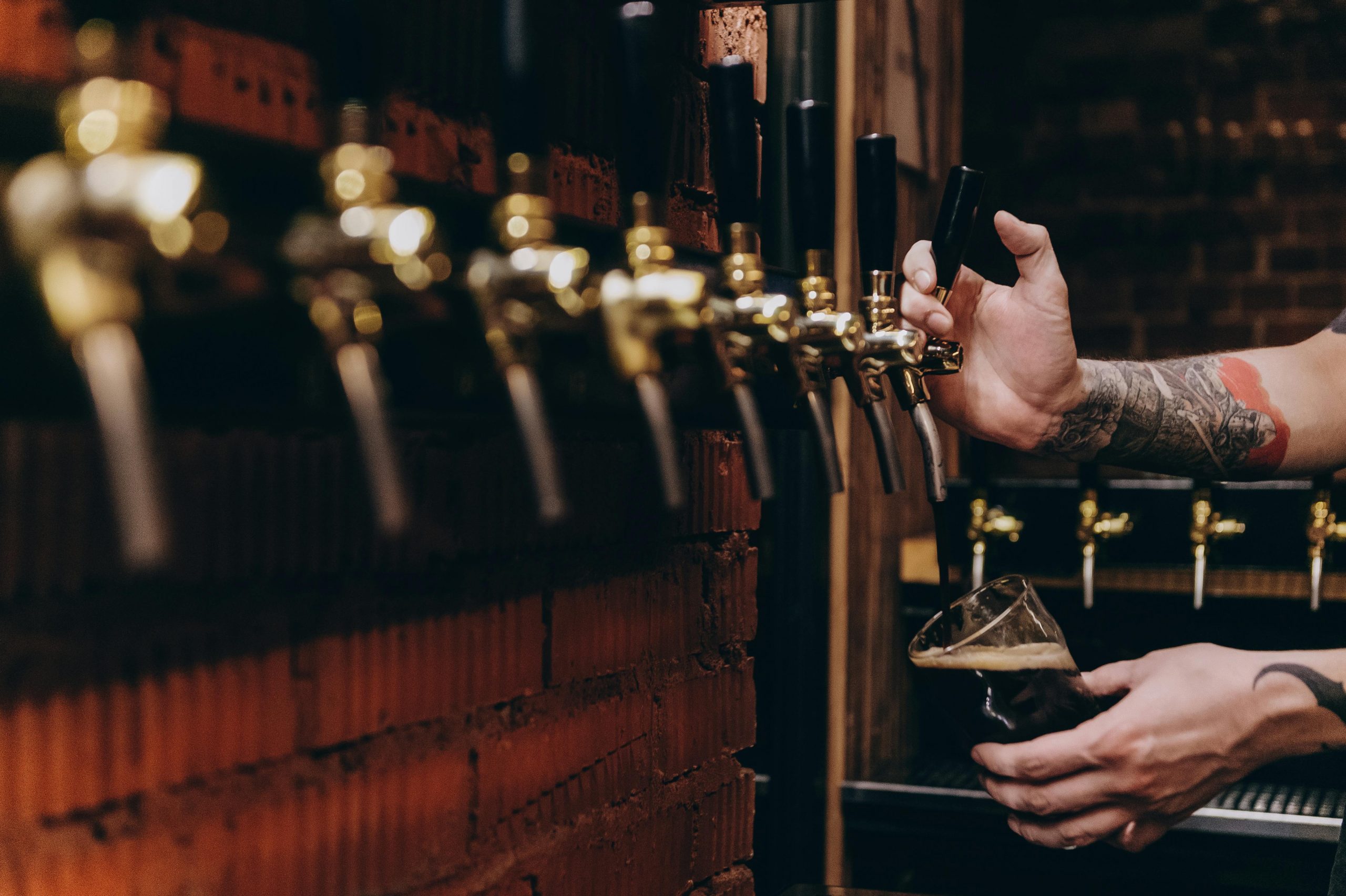 Close-up of beer being poured from a tap into a glass in a rustic pub setting.